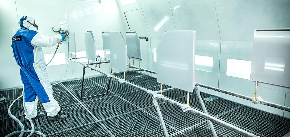 Technician spray-finishing aircraft interior panels in a controlled booth